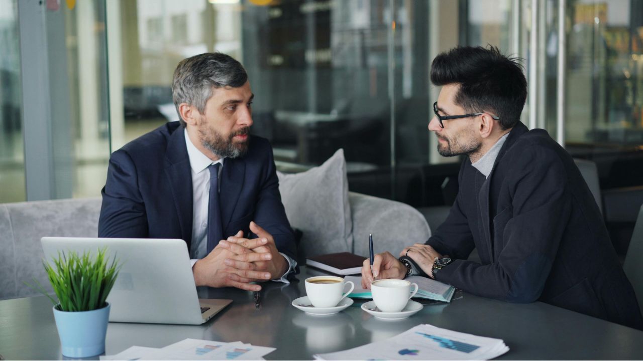 Two men discussing a business sale over a coffee